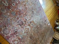 Full view of the large faded area rug on hardwood floor showing floral pattern and signs of wear