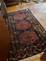 Full view of red and navy geometric area rug with three medallions and white fringe, placed on hardwood and atop larger faded rug