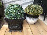 Two artificial round topiary plants side by side on wooden surface, showing contrasting pots and leaf coloration.