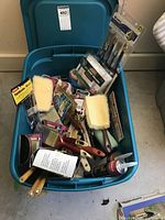 Blue tote filled with assorted new paint brushes, rollers, foam brushes, and adhesive.