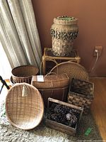 Seven woven baskets and wooden box arranged on floor and small bamboo/rattan stool against a wall, showing variety of sizes and shapes