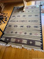 Full view of Navajo style blanket spread on floor showing geometric star and diamond patterns in earth tones with fringed edges.