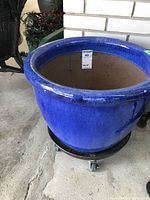 Front view of a large blue ceramic planter with a glossy finish sitting on a wheeled metal base.