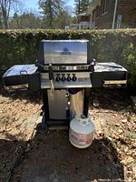 Front view of stainless steel Broil King Crown gas grill on cart with propane tank attached and side shelves