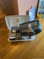 Plastic bin containing Sony portable CD player with attached headphones and various CDs in jewel cases inside, placed on wooden floor.