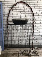 Full view of metal garden trellis with planter box, showing the arch shape and decorative wrapped beads, set against a brick background.
