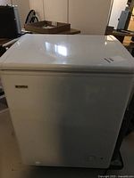 White Kenmore chest freezer with closed lid in basement setting.