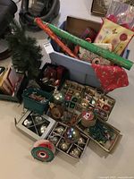 Christmas decorations including multiple boxes of glass ball ornaments, rolls of gift wrap, artificial tree, and gift bags.