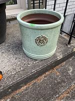 Front and angled view of light green clay patio planter with circular floral emblem on the front.