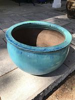 Full view of round teal clay planter with wide rim on concrete surface in outdoor setting.