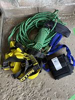 Overview photo showing coiled green climbing rope, yellow and black Miller climbing harness, blue lanyards, and protective sleeve.