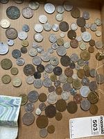 Top view of many mixed coins laid out on brown cardboard, showing variety and quantity.