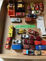 Overhead photo of all toy vehicles in cardboard box, showing variety of cars and construction vehicles.