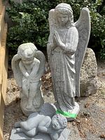 Three concrete angel statues - tall praying angel, seated winged angel, and sleeping winged angel.