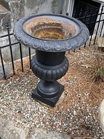 Full side view of the black concrete urn planter positioned outdoors showing its overall shape and ornamental relief detailing.