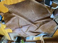 Top view of the large brown cowhide rug laid out flat, showing its full size and shape on a wooden floor.
