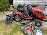 Side view showing red body, black seat, rear tire, missing grass bag, tools on ground.