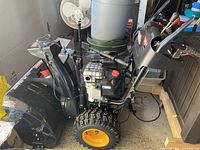 Left-side view of snowblower showing engine block, handlebar controls and large treaded wheels