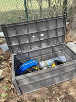 Plastic outdoor deck box open showing contents inside including ropes, fencing, extension cord and tarp.