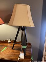 Full view of the decorative table lamp showing beige lampshade and dark wood tripod base on wooden table.