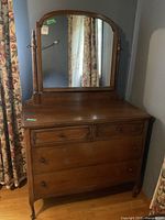 Full view of the wooden dresser with four drawers and attached swing mirror in a room with floral curtains.