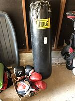 Full view of black Everlast heavy bag with chain, two pairs of boxing gloves in front on the floor, and speed bag nearby