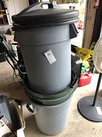 Stacked three large plastic garbage pails, two have black covers, one has a green inner ring.