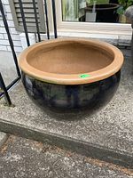 Large round garden planter with glossy black exterior and unglazed tan rim, shown on concrete surface.