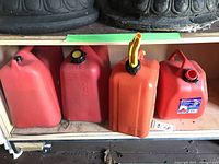 Photo showing four different plastic gasoline jerry cans on a shelf, with two black pots above them.