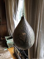 Side angle view of the pierced hanging metal lamp showing teardrop shape and decorative patterns