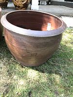 Front and side view of large round clay planter on grass, showing its shape, surface, and minor wear.