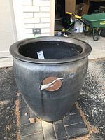 Full view of large black oval clay planter on outdoor paving, showing overall shape and decorative front feature.