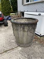 Full side view of a large resin urn placed on a concrete surface outdoors, showing overall shape and weathered exterior.