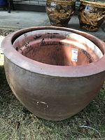 Front view of large round clay planter with plastic insert showing exterior and partial interior with sticker