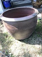 Side view of large round clay planter showing shape, size, and color under sunlight outdoors.