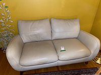 Front view of ivory leather two seater loveseat with two cushions and curved armrests set against a yellow wall.