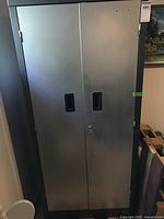 Front view of the gray metal storage cabinet with two doors and black recessed handles.