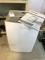 Photo showing white NOMA dehumidifier with instruction manual placed on top, highlighting overall design and condition.