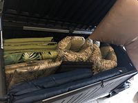 Photo showing stacked outdoor chair cushions including green and beige leaf patterned cushions, navy blue cushions, and beige cushions.