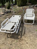 Photo of white patio chair and matching lounger set outdoors on dirt ground.