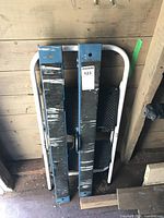 Top view of folded portable sawhorses and two step ladder, showing the worn blue sawhorses and white ladder frame with black steps.