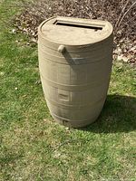 Beige plastic rain barrel with textured surface and top lid on grass.