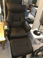 Front view of black leather reclining armchair with matching ottoman on light-colored floor