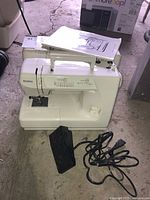 Front view of Kenmore sewing machine with foot pedal and power cord on floor beside it.
