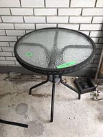 Full view of small round glass top bistro table with metal frame and tripod legs.