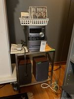 Photo shows full stereo component system on metal stand with speakers below and basket with CDs and tapes on top.