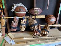 Basketball, football, baseball gloves, wooden bat, and hockey sticks arranged on racks