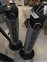 Two black and silver Airworks tower oscillating fans side by side on floor