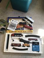 Overview of train set components in original packaging including locomotive, freight cars, tracks, lights, instruction manual, and transformer.
