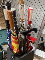Six golf umbrellas standing in a container. Handles made of wood and plastic with colorful canopies.